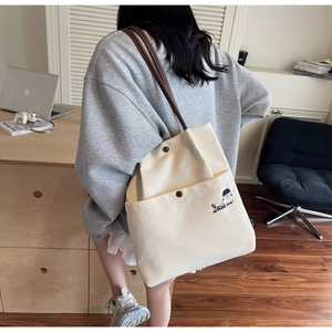 Detailed view of cream canvas tote bag with brown straps and cute girl embroidery