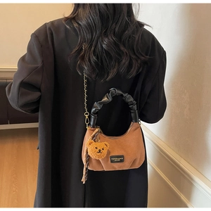Detailed close-up of brown suede crescent bag with pleated handle and cute bear charm