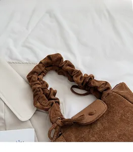 Detail of soft scrunchie shoulder strap and brown suede texture on a stylish bucket bag