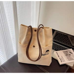 Detailed view of the off-white canvas tote bag featuring fine embroidery and leather handles