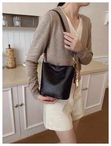 Détail d'un sac seau en cuir noir avec pompon en perles sur la bandoulière réglable
