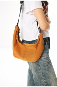 Side view of lightweight orange crescent hobo bag worn with adjustable black shoulder strap