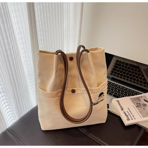 Detail of canvas tote bag with Docile Girl embroidery and brown handles in home setting