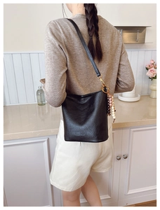 Détail du sac seau en cuir noir avec ferrures dorées et breloque en perles de style ethnique