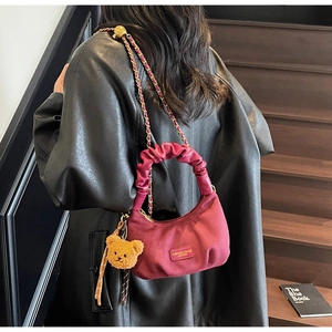 Detail of burgundy hobo bag with pleated handle, gold chain strap and teddy bear charm