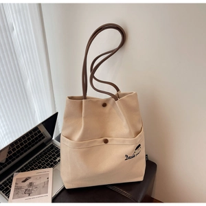 Detail of beige canvas tote bag featuring Docile Girl embroidery and brown shoulder straps