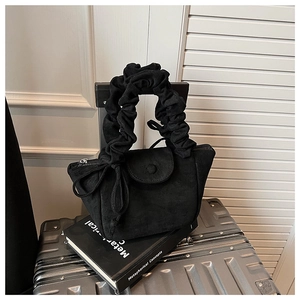 Close-up of black suede handbag featuring a pleated scrunchie handle and bow detail