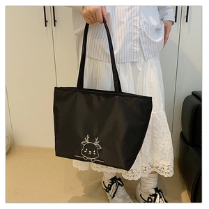 Detail view of a black nylon tote bag featuring a white embroidered cartoon deer pattern