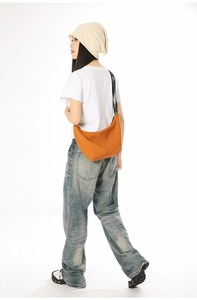 Orange moon-shaped crossbody bag worn by a model in a casual streetwear style