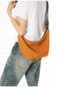 Detail of orange nylon crescent crossbody bag featuring adjustable black shoulder strap