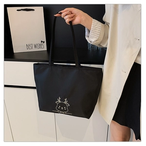 Detail of a black canvas tote bag featuring a minimalist white embroidered deer pattern
