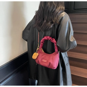Burgundy crossbody bag with pleated handle and cute bear charm shown on black leather jacket