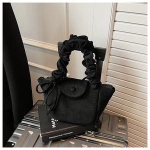 Close-up of black faux suede bucket bag featuring scrunchie handle and drawstring details
