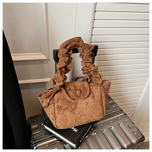 Detail view of brown faux suede handbag with a pleated cloud handle on a silver suitcase