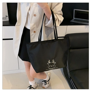 Detail view of the black canvas tote bag with white cartoon deer embroidery in a workplace setting