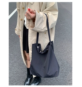 Photo lifestyle d'un grand sac cabas en nylon noir associé à un trench-coat beige