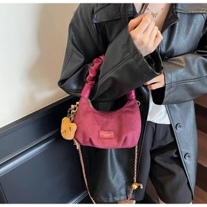 Detail of burgundy hobo bag with pleated handle, chain strap, and plush bear charm