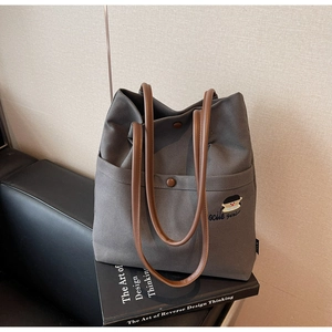 Close-up of charcoal canvas tote bag with brown leather straps and embroidered character