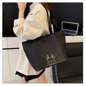 Close-up of black canvas tote bag with white embroidered deer pattern in office setting