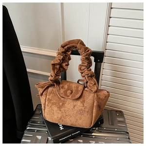 Detail of a brown suede handbag with pleated handle and button closure on luggage