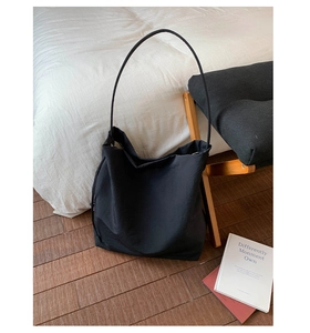 Vue détaillée du grand sac cabas noir minimaliste posé sur une parure de lit blanche
