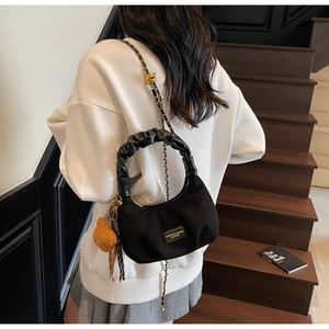 Detail of black crescent handbag featuring a pleated handle and golden chain strap
