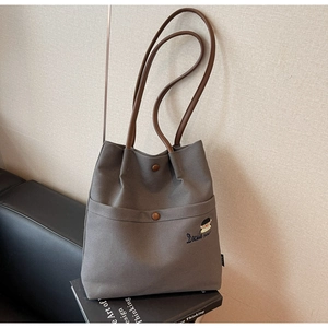 Detail of gray canvas tote bag featuring Docile Girl embroidery and brown leather straps