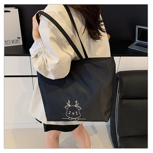Detail of deer embroidery on a black canvas tote bag carried by a model in an office setting