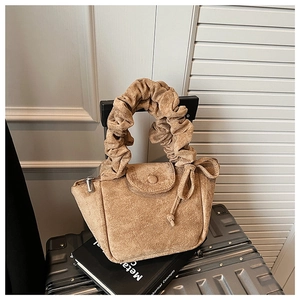 Detail of khaki suede handbag with scrunchie handle on minimalist travel suitcase