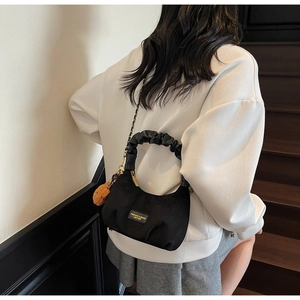 Detail of black dumpling bag with pleated handle, metal chain, and cute bear charm
