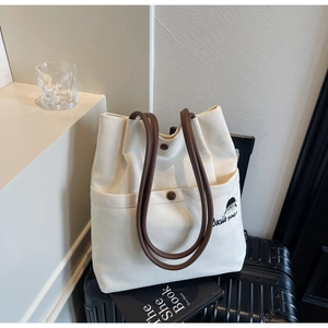 Detail view of canvas tote bag featuring brown leather handles and bird embroidery detail