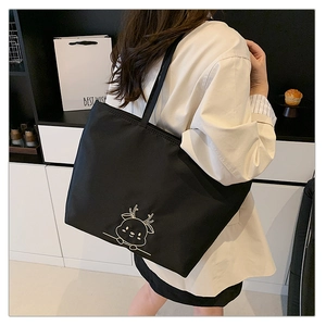 Detail of deer embroidery on a black canvas tote bag worn by a model in a lifestyle setting