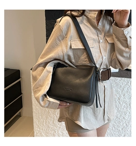 Detail shot of a black minimalist leather bucket bag worn by a model in a modern interior