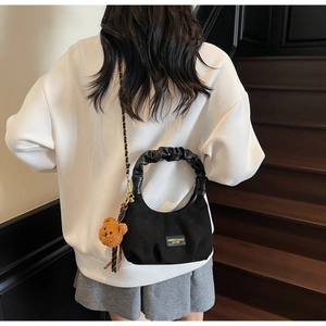 Detail view of black suede dumpling bag featuring pleated handle and brown bear plush charm