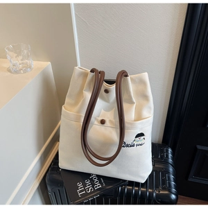Detail of canvas tote bag with brown leather handles and Docile girl embroidery