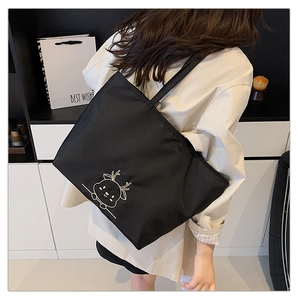 Rear view of a black canvas tote bag with white deer embroidery on a female model