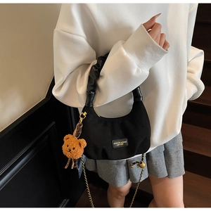 Detail of black crescent hobo bag with pleated handle, gold chain and teddy bear charm