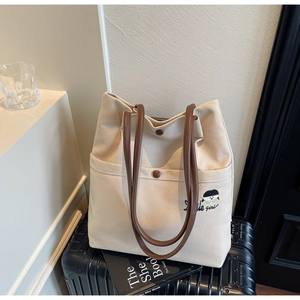 Detail of off-white canvas tote bag featuring embroidery and brown leather shoulder straps
