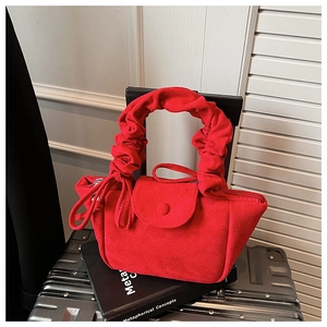 Close-up of red suede handbag with pleated cloud handle on black luggage case