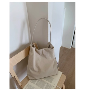 Sac fourre-tout beige minimaliste sur une chaise en bois à côté d'un livre ouvert