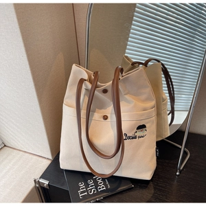 Close-up of beige canvas tote bag featuring brown leather handles and girl embroidery