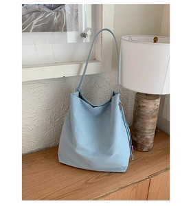 Détail du sac hobo en toile bleu clair montrant le cordon latéral et l'étiquette rose sur bois