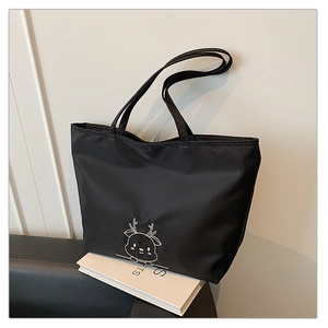 Detail view of cartoon deer embroidery on black nylon tote bag against a sofa background