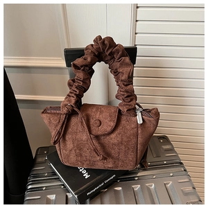 Detail of coffee brown suede pleated tote bag with cloud handle on a suitcase