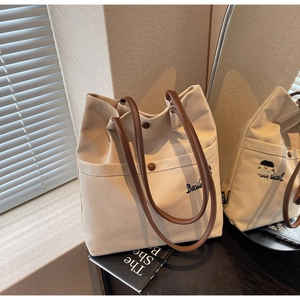 Detail of canvas tote bag showing Docile embroidery and leather handles in a mirror view