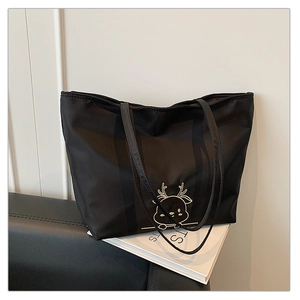 Detailed view of black nylon tote bag with white cartoon deer pattern on a magazine