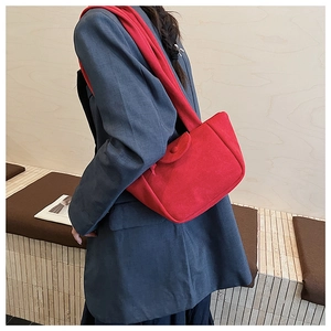Detail view of a vibrant red pleated bucket bag worn by a model in a grey suit
