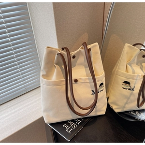 Detailed close-up of cream canvas tote bag with brown leather straps and embroidery