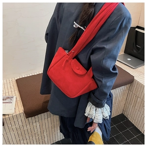Detail of red suede bucket bag with wide shoulder strap worn with navy blazer