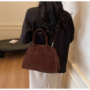 Détail d'un sac cabas marron rétro en daim porté par un mannequin dans un décor moderne